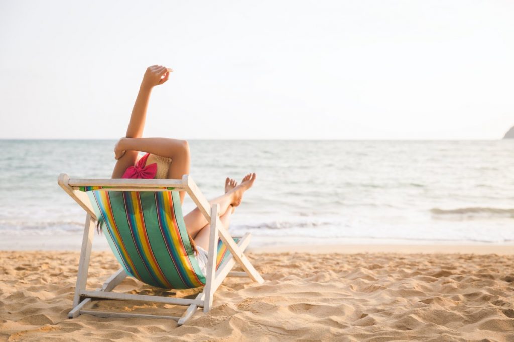 Woman subathing by the ocean in a striped chair