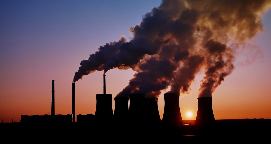 Smoke stacks from power plants silhouetted against a sunset.