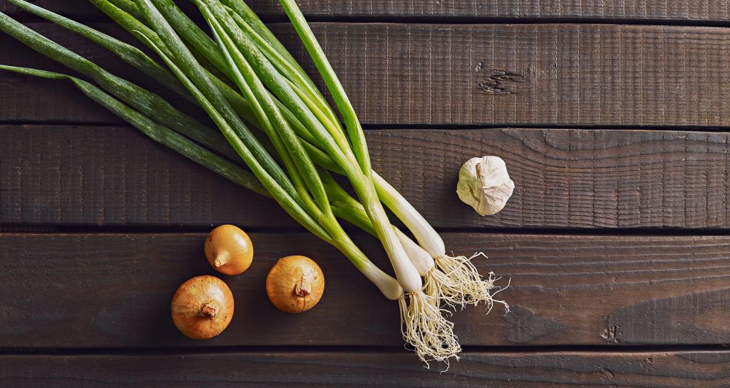 garlic bulb, green onion, and onion bulbs on a table