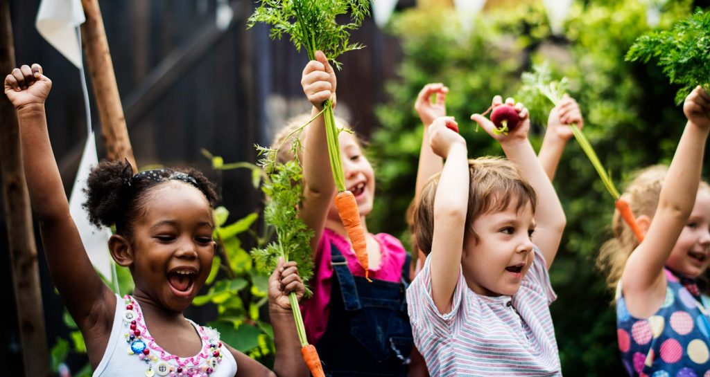 kids excitedly holding carrots with their arms up