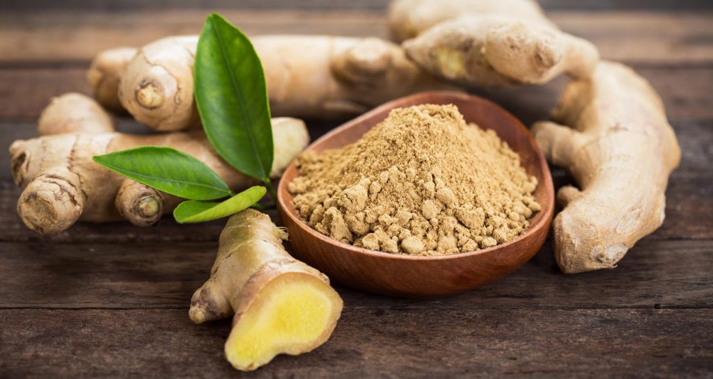 ground ginger in a bowl next to ginger root