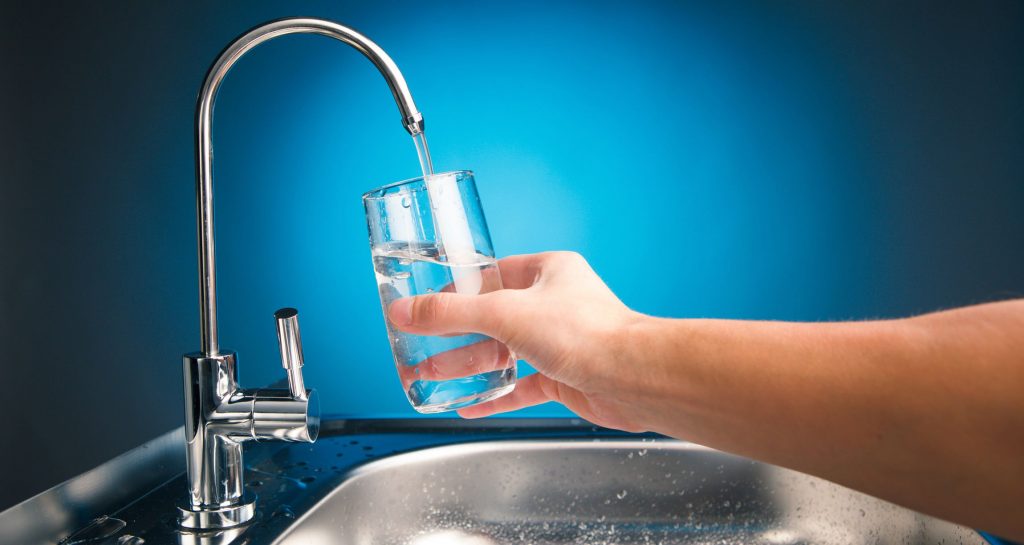 drinking glass being filled from a sink faucet